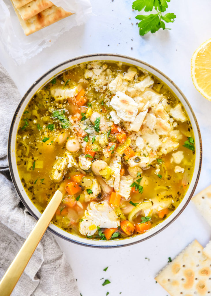 white bean lemon chicken soup in a bowl with saltine crackers on top.