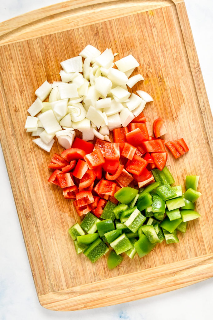 roughly cut bell peppers and white onion on a cutting board.