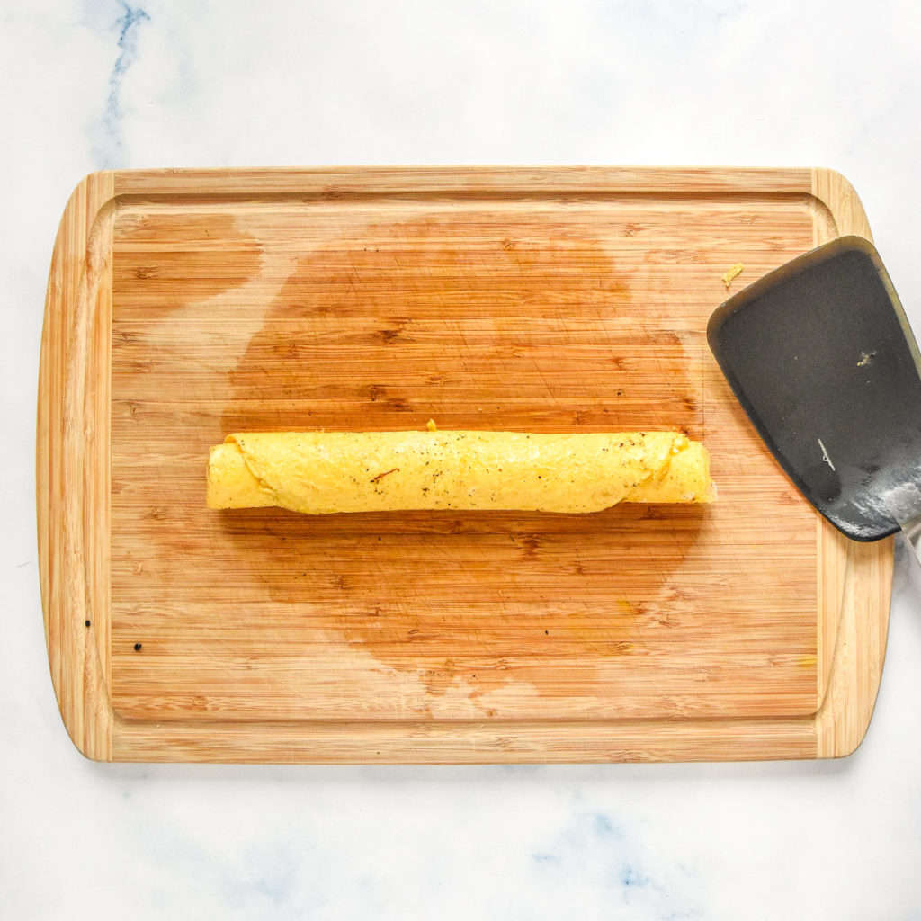 an egg pancake rolled up on a cutting board.