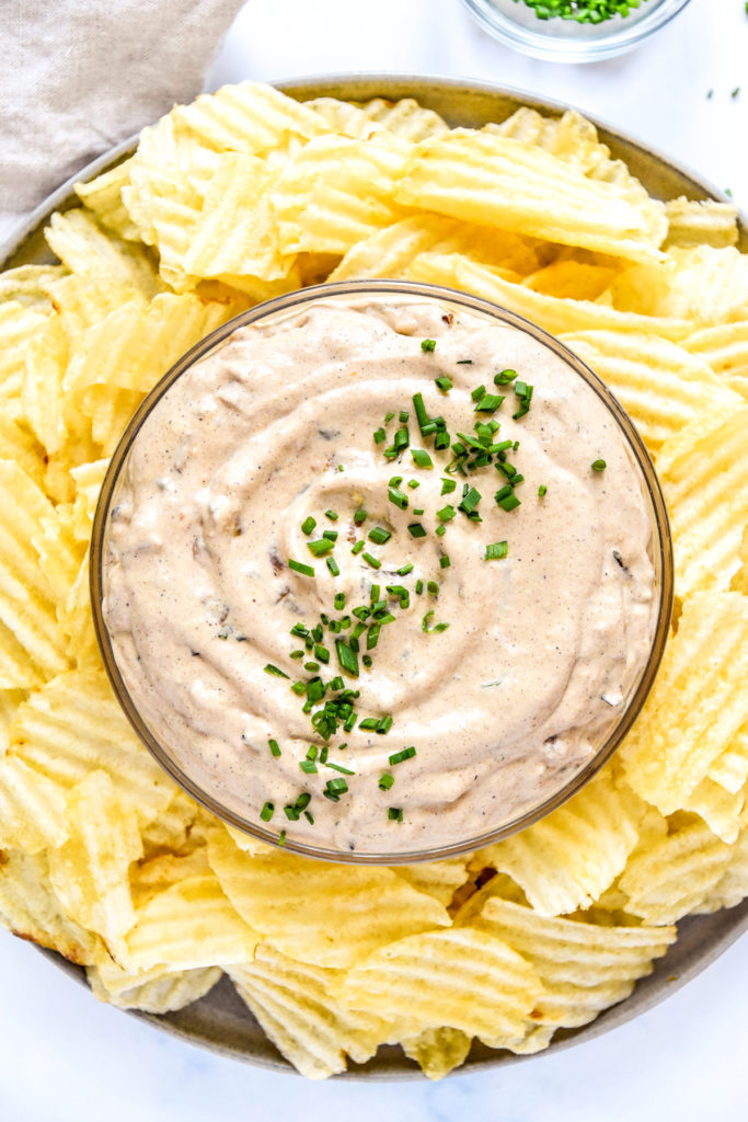 homemade roasted onion dip in a bowl with chives and potato chips on the side.