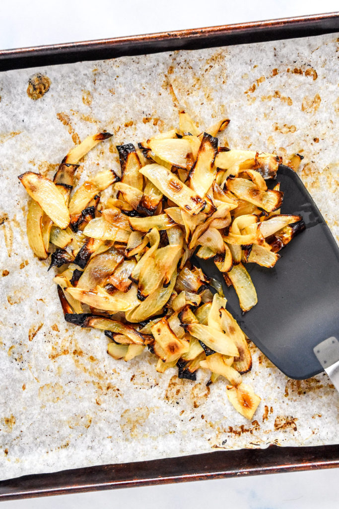 roasted onions on a sheet pan with a spatula.