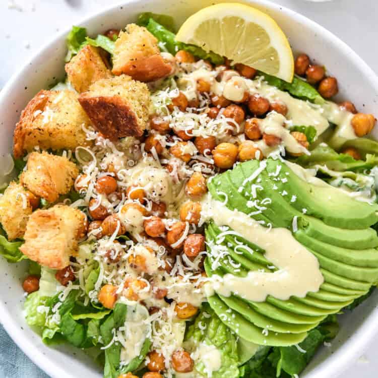 roasted chickpea caesar salad with avocado and croutons in a white bowl.