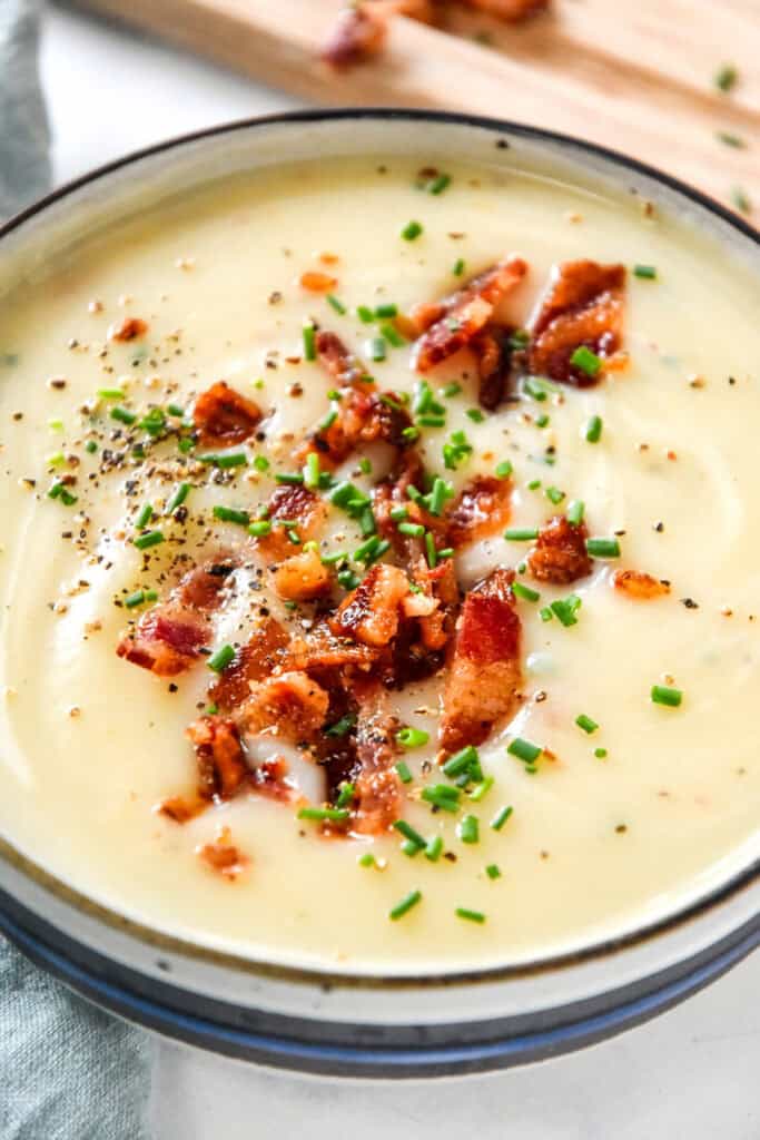 close up of creamy potato onion soup with bacon bits and chopped chives on top.