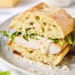 caesar salad chicken sandwiches on a plate cut in half with dressing dripping.