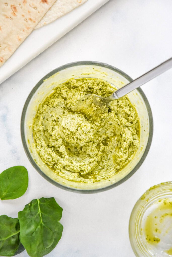cream cheese and pesto mixed in a glass bowl.