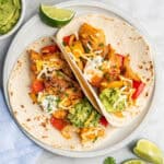air fryer chicken fajitas on flour tortillas with sour cream and guacamole on top.