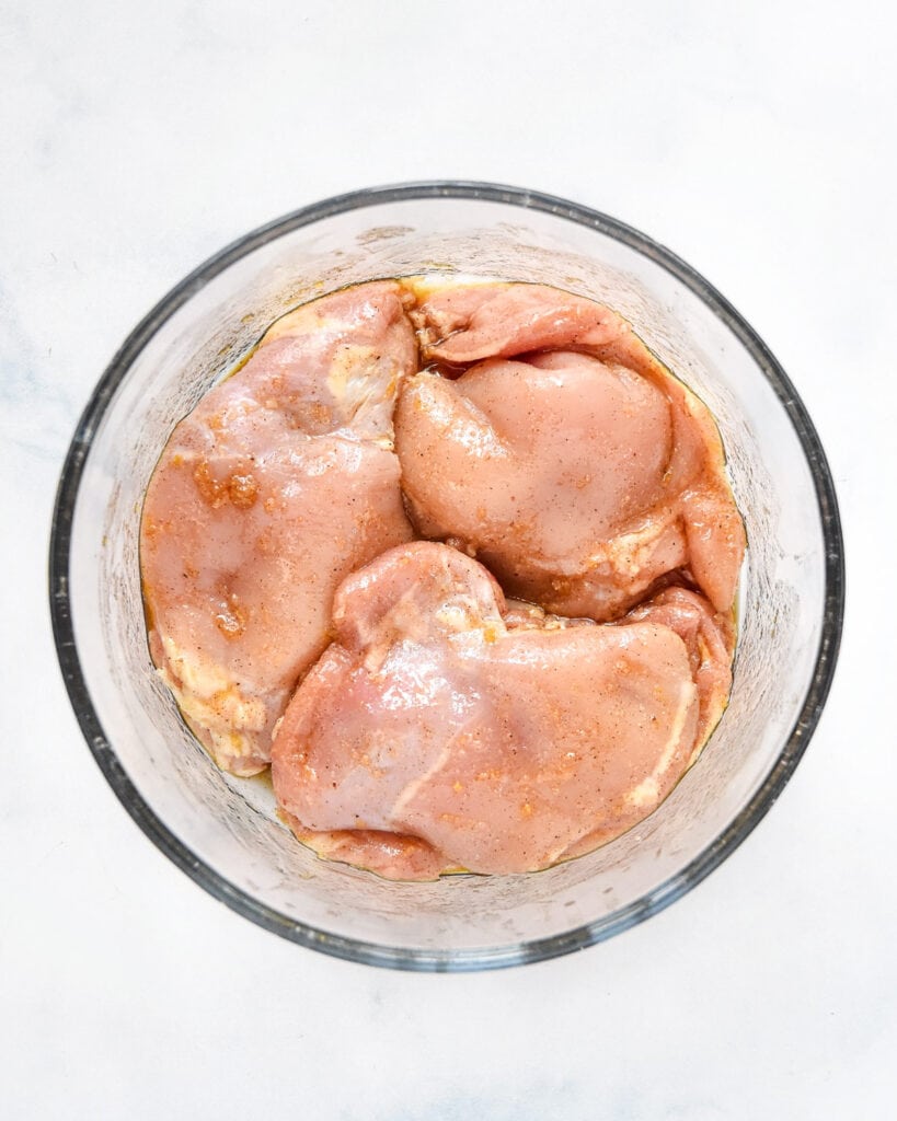 chicken thighs marinating in a bowl before cooking.