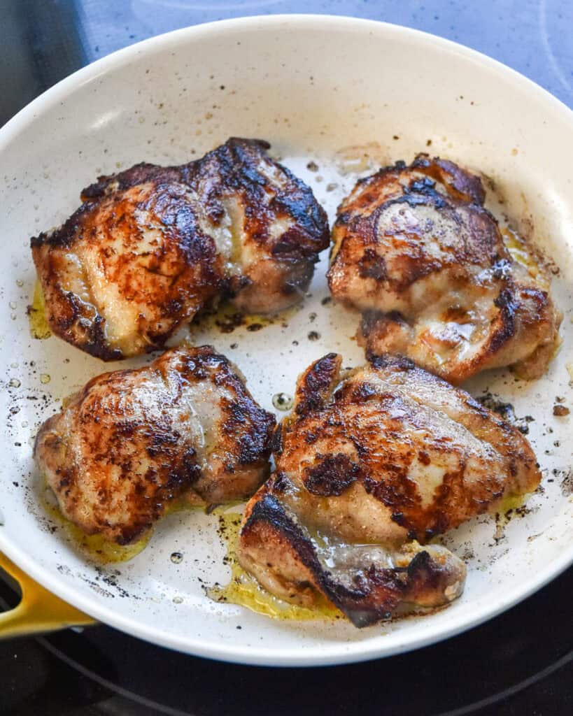 spiced chicken thighs cooking in a pan.