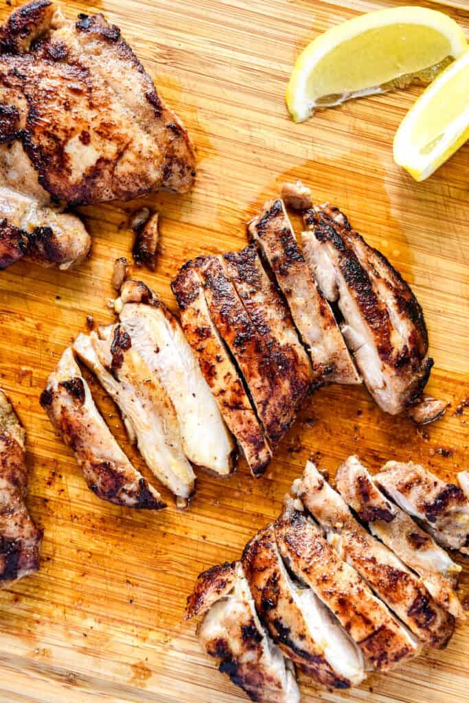 cooked and sliced spiced chicken thighs on a cutting board before serving.
