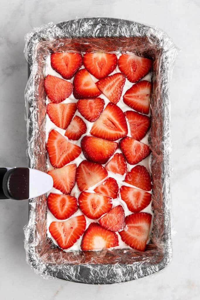 a layer of sliced strawberries on top of whipped cream in a loaf pan.