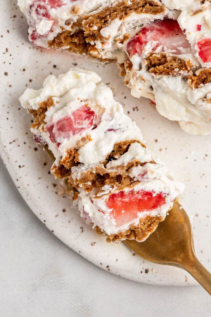a bite of strawberry gingersnap icebox cake on a gold fork on a white plate.