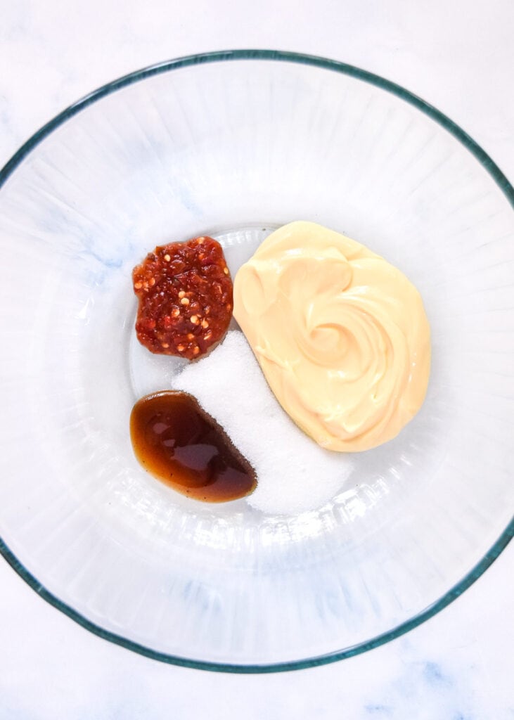 kewpie mayo and sauces in the bottom of a large glass bowl.