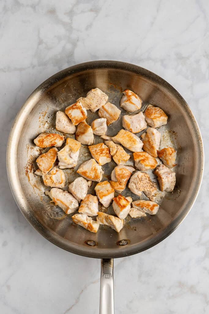 browned chicken pieces in a stainless steel skillet.