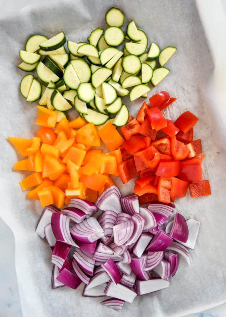 cut peppers, zucchini and onions on a parchment paper lined sheet pan.