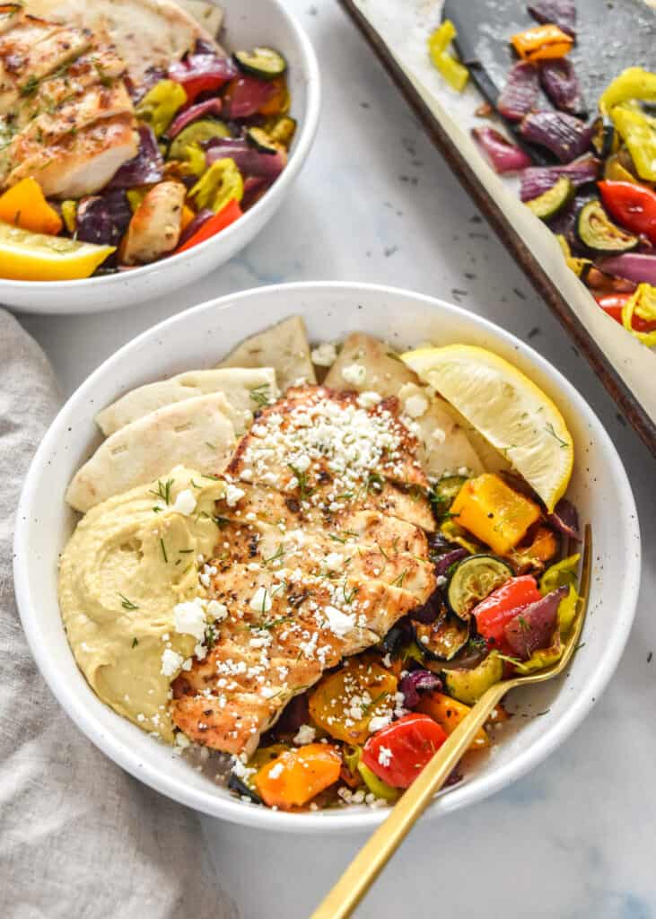 Easy Oven Roasted Summer Vegetables in bowls with sliced chicken, hummus and pitas.