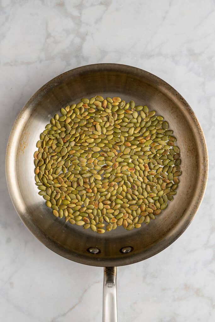 pepitas pumpkin seeds toasting in a skillet to golden brown.